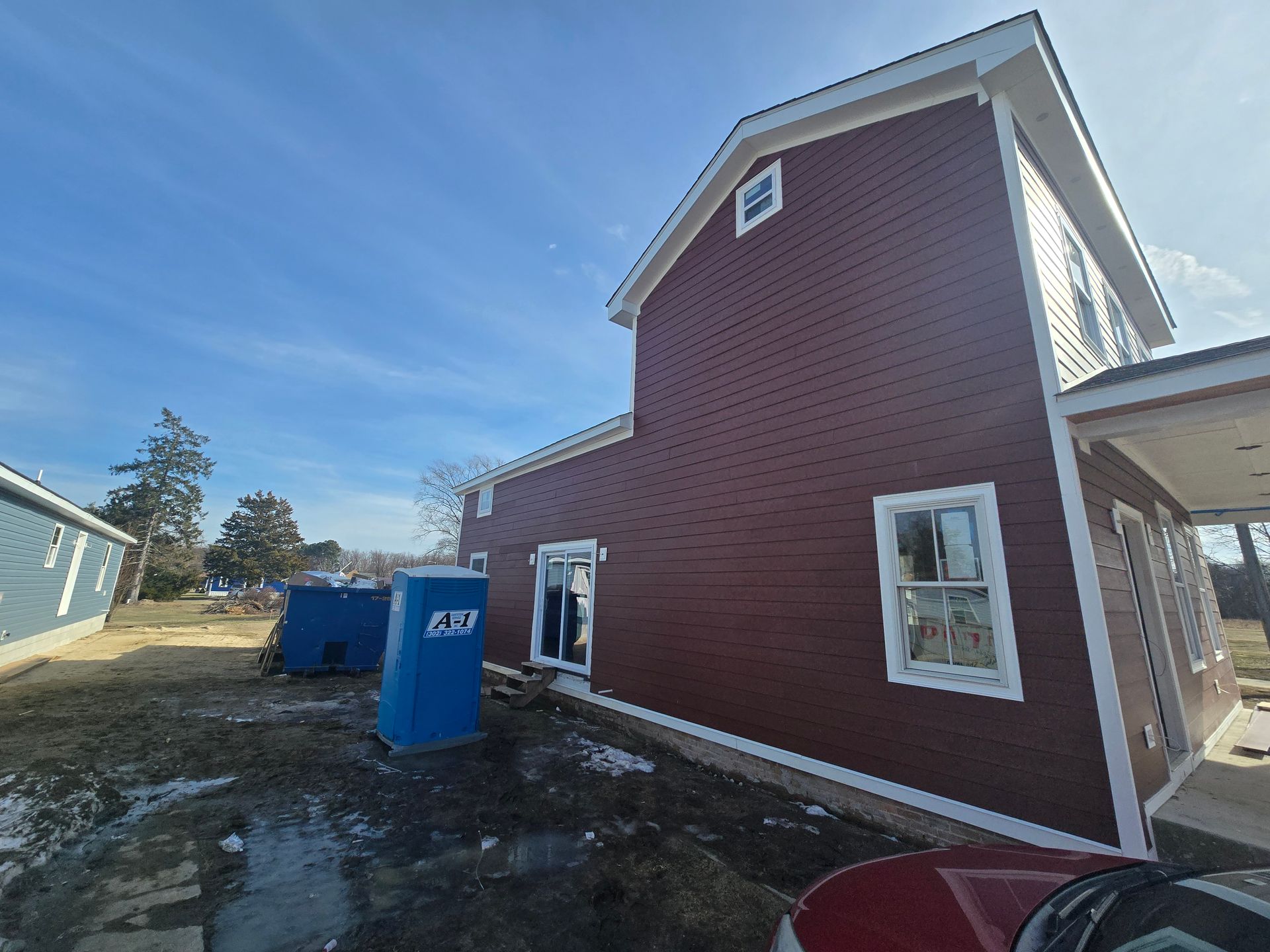 A red house with a blue portable toilet in front of it.