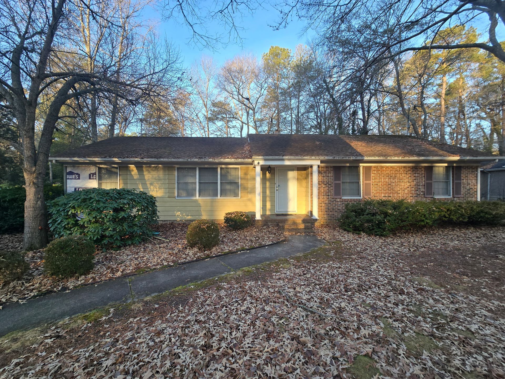 A brick house with a walkway leading to it is surrounded by trees and leaves.