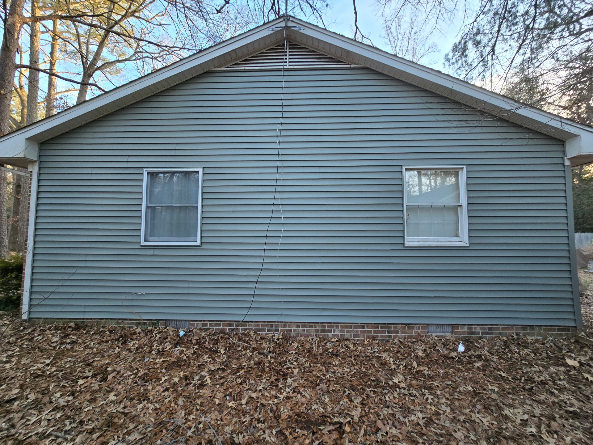 The back of a house with a lot of leaves on the ground.