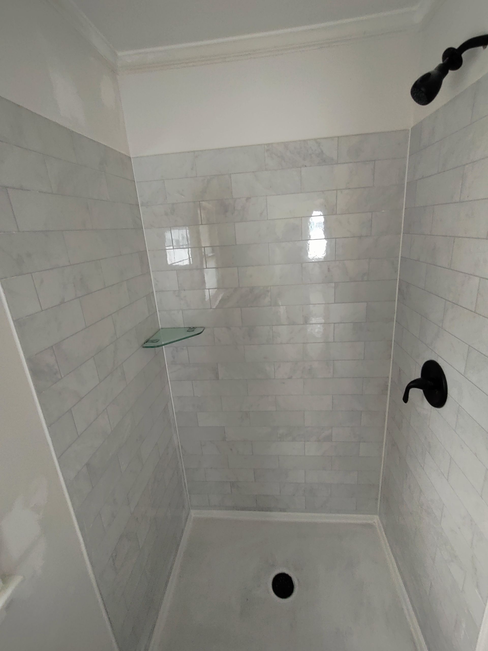 A shower with white tiles and a black shower head.