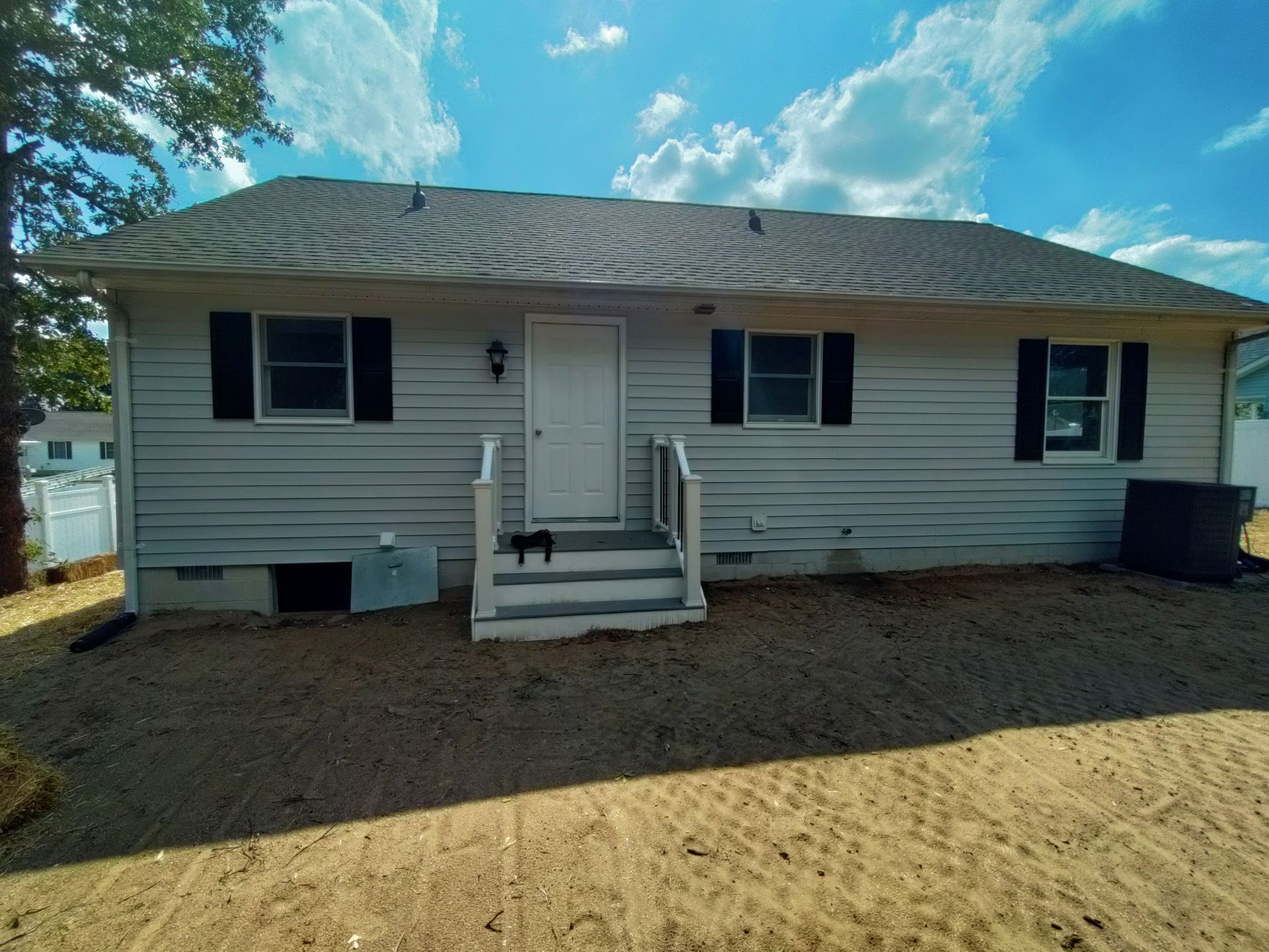 A white house with black shutters and a dog on the porch