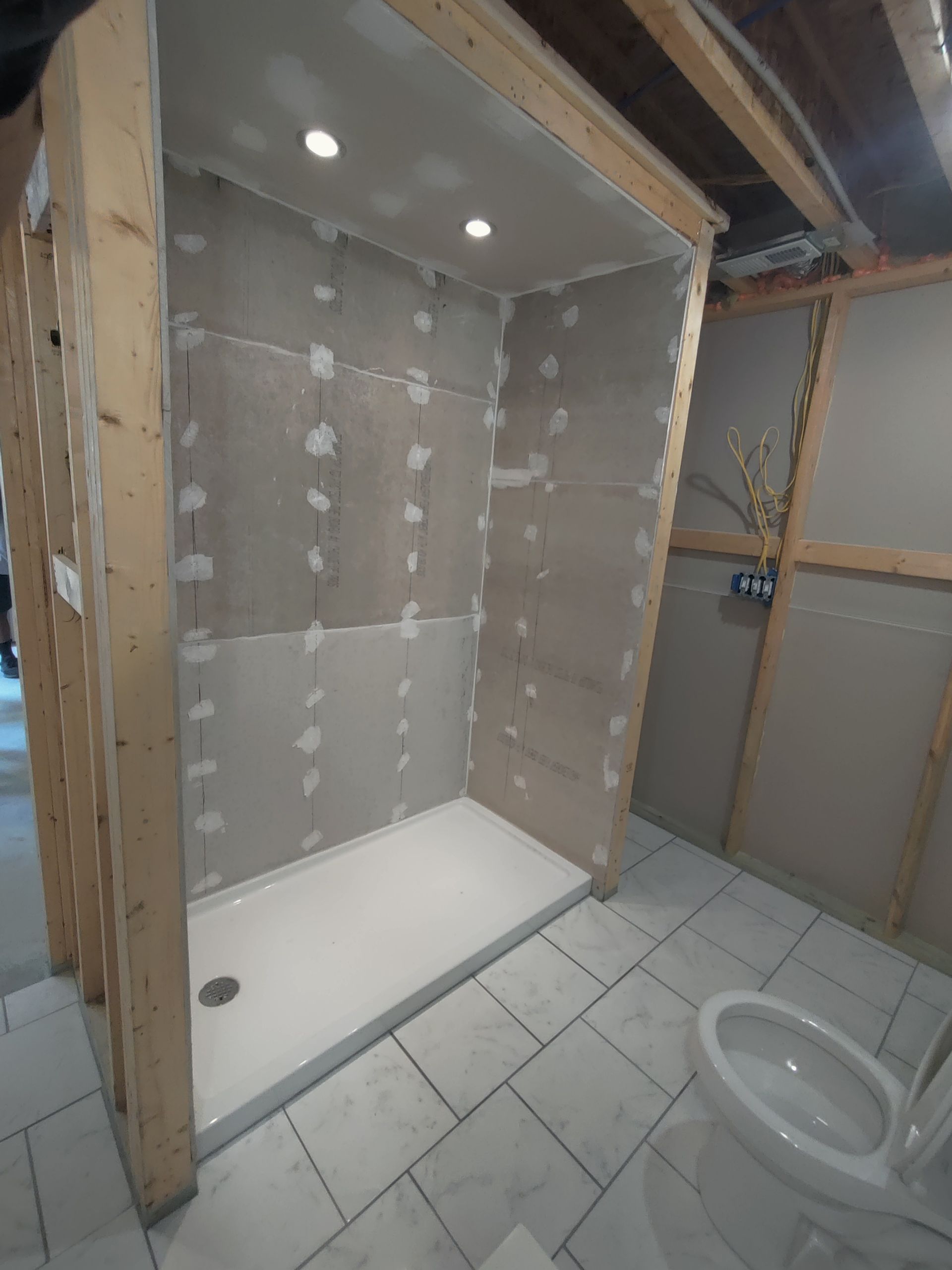 A bathroom with a toilet and a shower stall under construction.