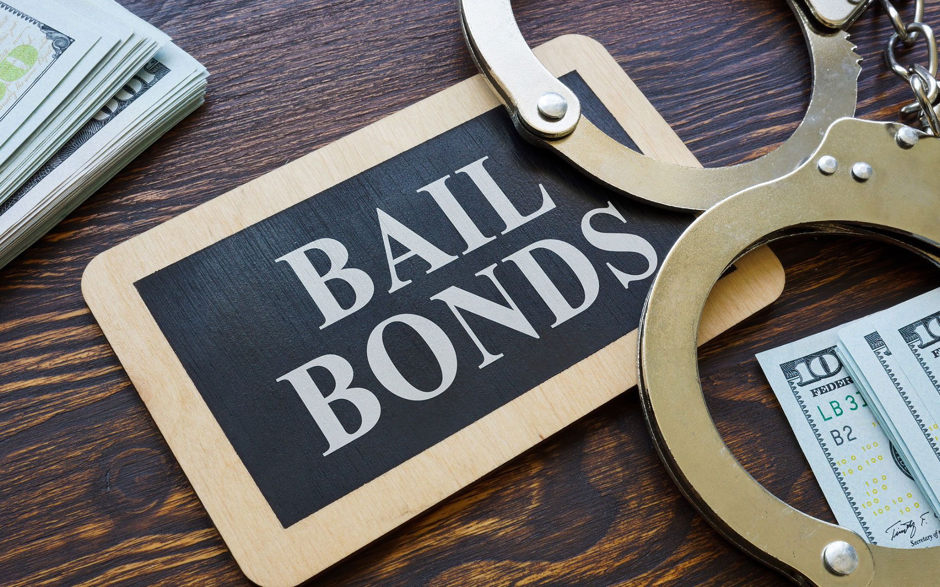 A sign that says `` bail bonds '' next to handcuffs and money on a wooden table.
