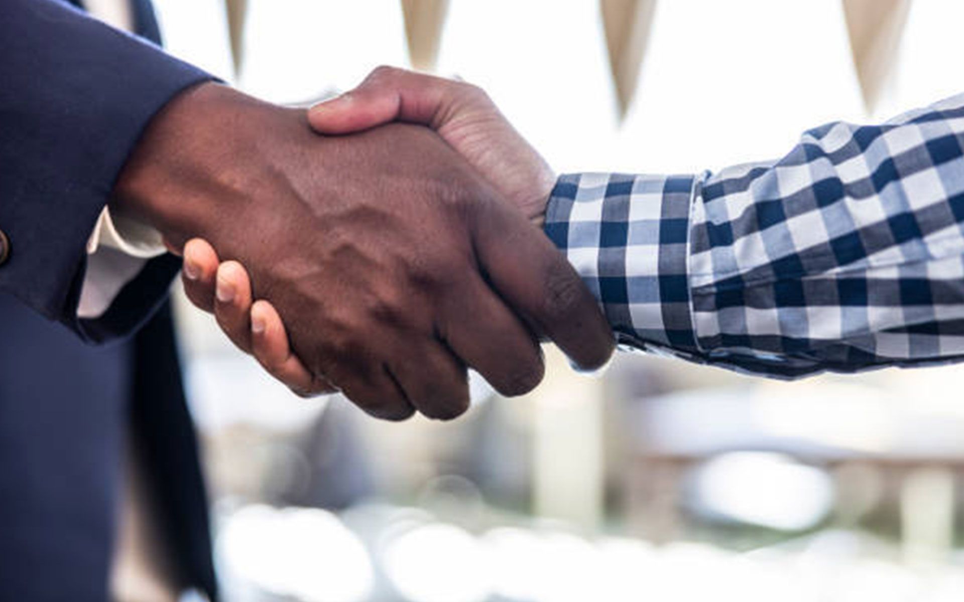 Two men are shaking hands in front of a window.