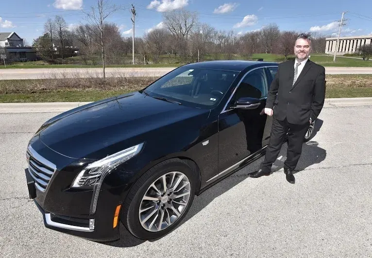A man in a suit and tie is standing next to a black car.