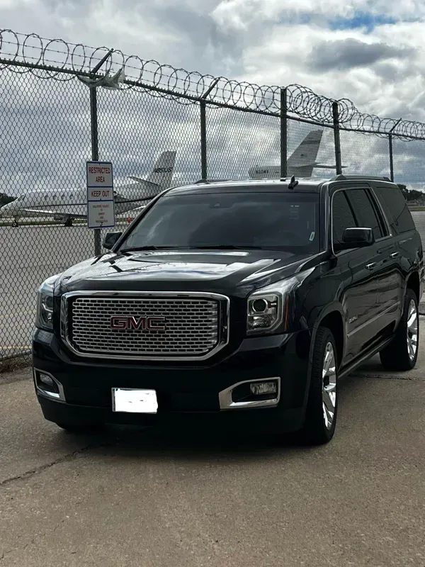 A black gmc yukon suv is parked in front of an airport fence.