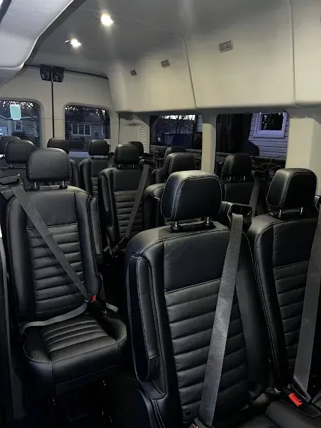 The inside of a bus with black seats and seat belts.