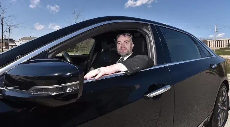 A man in a suit and tie is driving a black car.