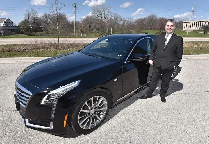 A man in a suit and tie is standing next to a black car.