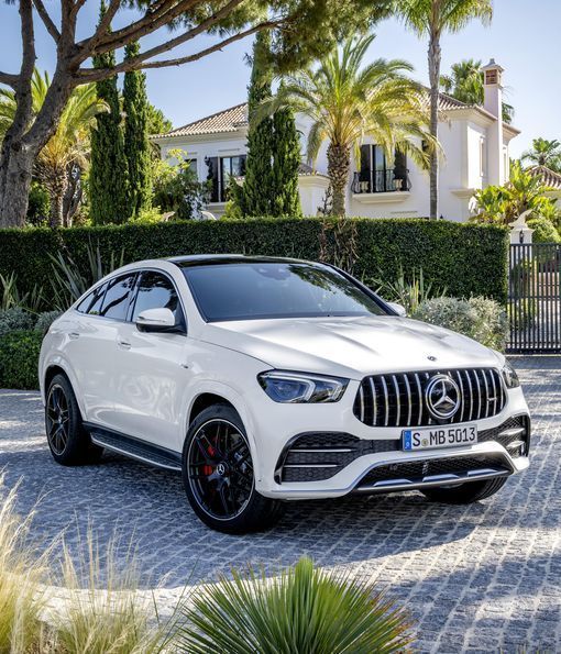 White Mercedes-Benz SUV parked on a cobblestone driveway in front of a luxury house with palm trees