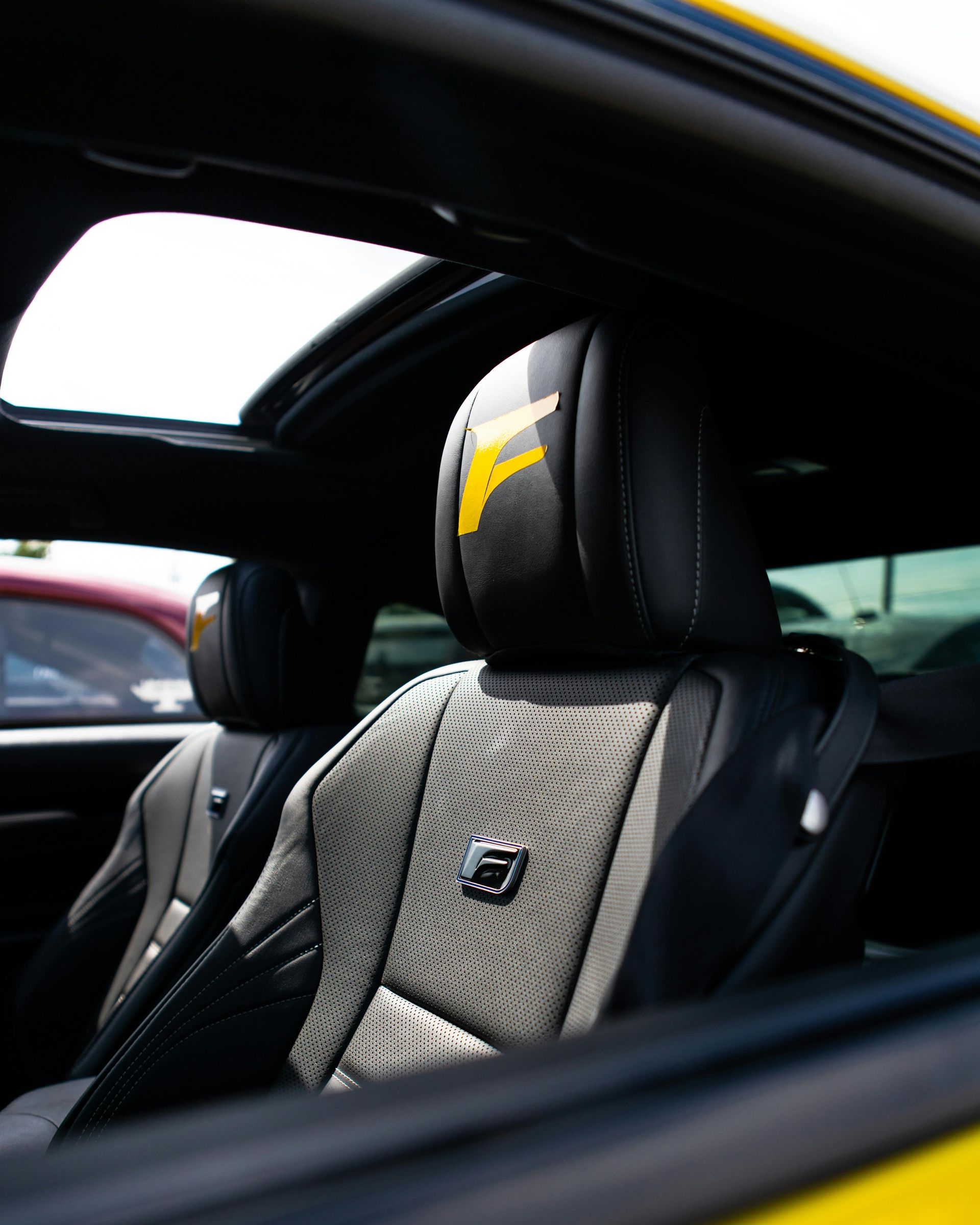 The inside of a car with black leather seats and a sunroof, highlighting a sporty design.