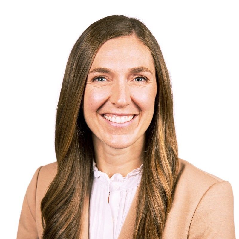 Woman with long brown hair smiling, wearing a light-colored blazer and shirt.