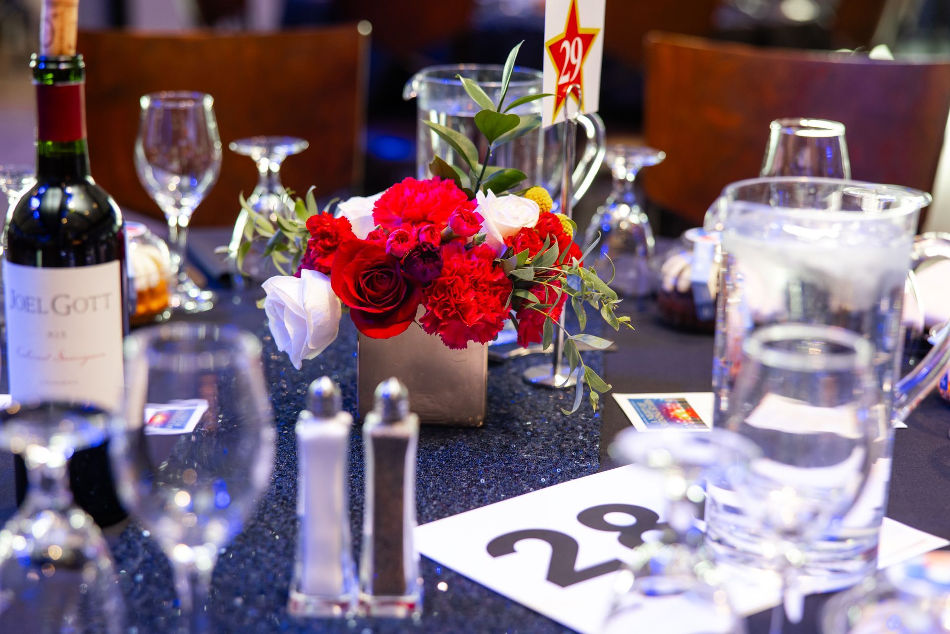 Table setting with wine, flowers, water pitchers, glasses, and a table number.