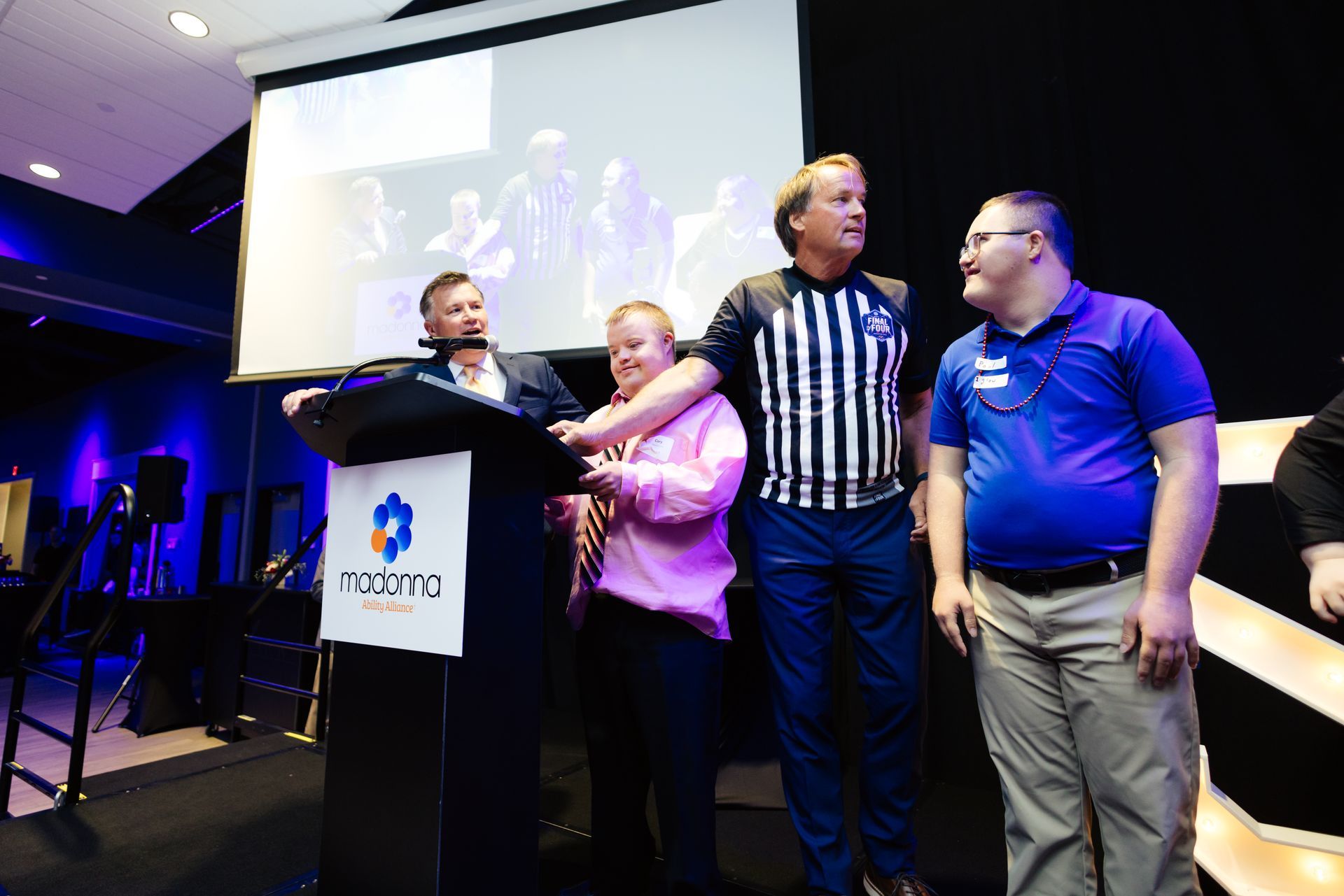 Four people on a stage with a man speaking at a podium.