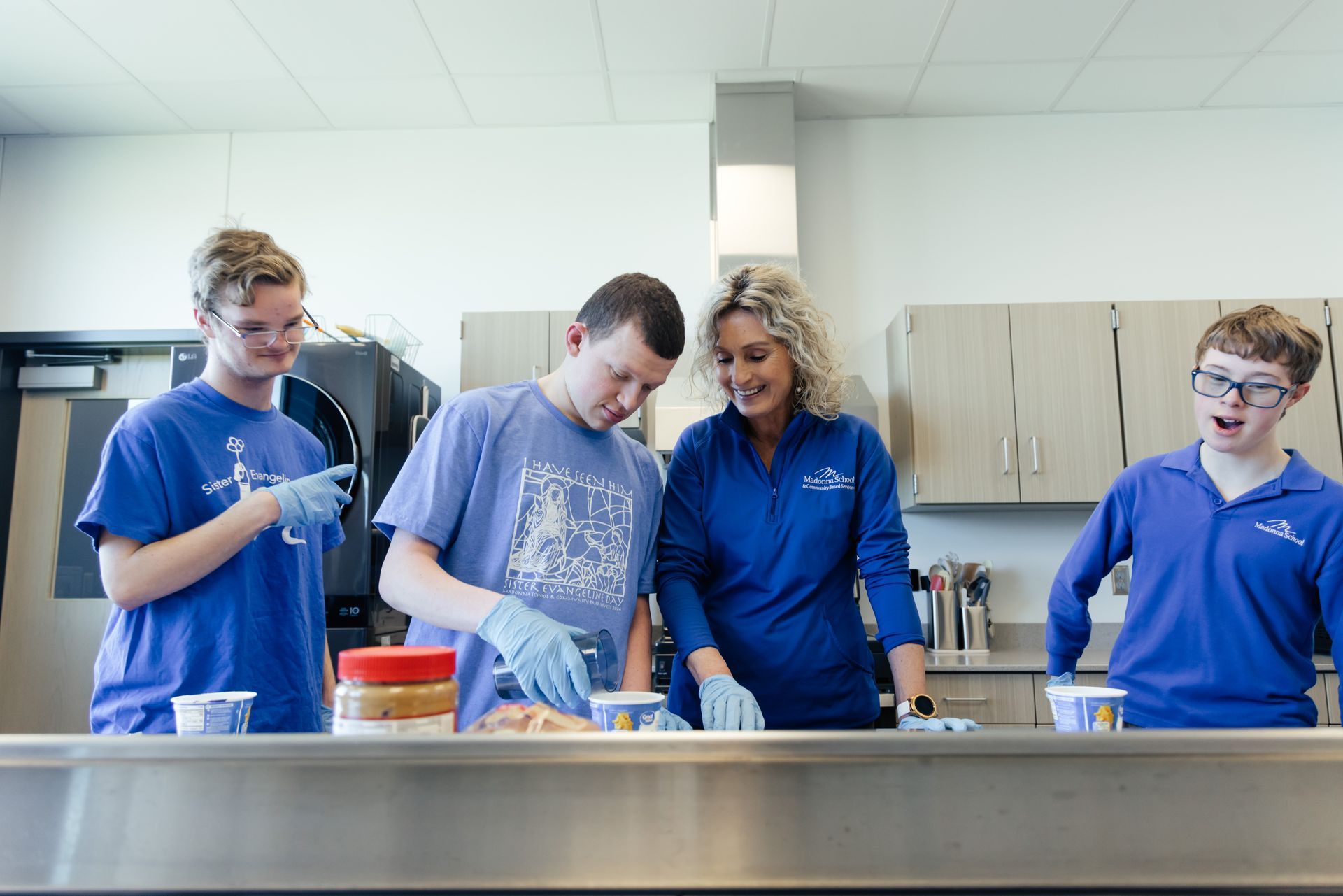Four people in blue shirts prepare food in a kitchen.