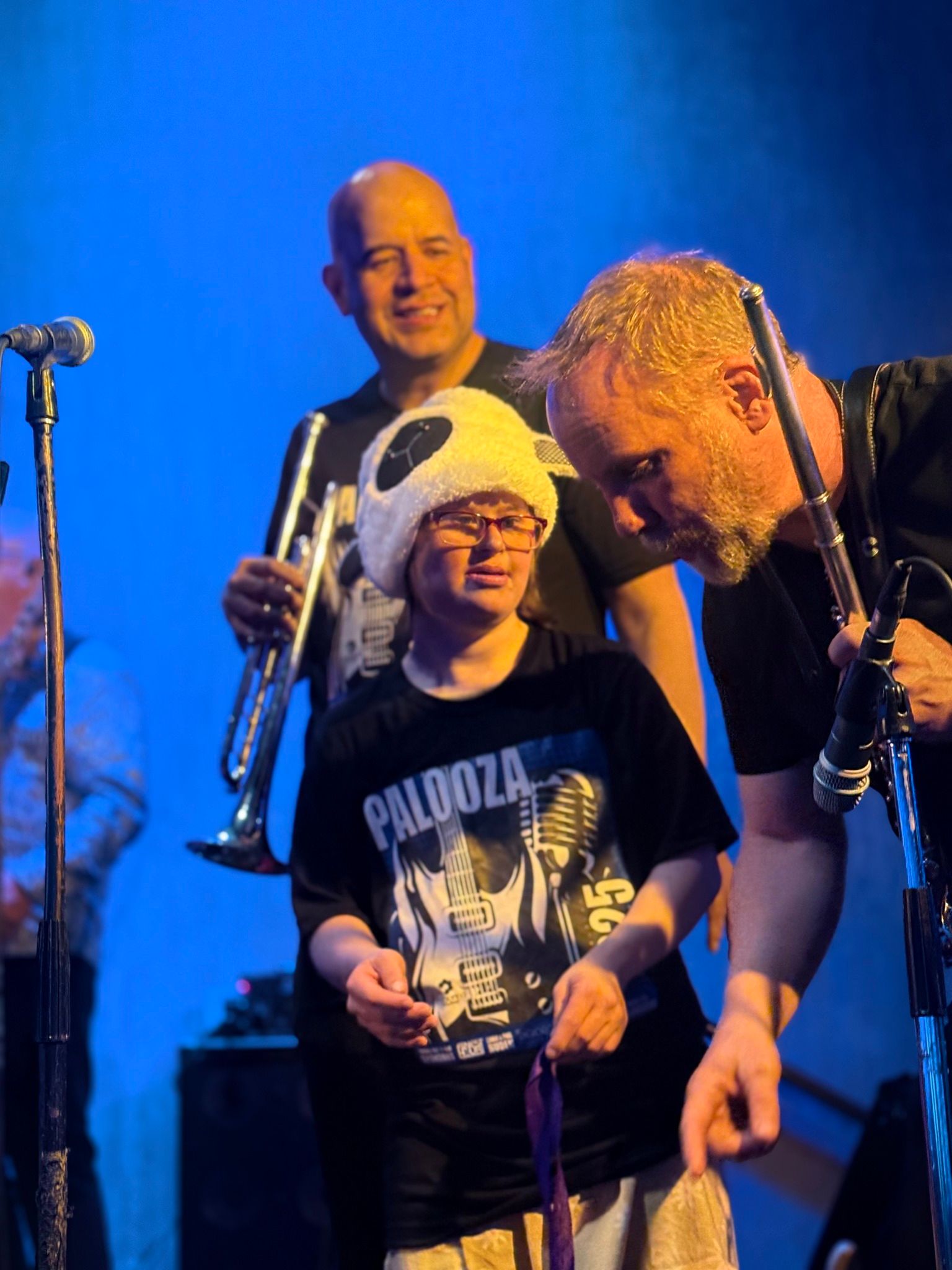 Band members on stage with a person in a panda hat. Blue background. One man holds a trumpet.