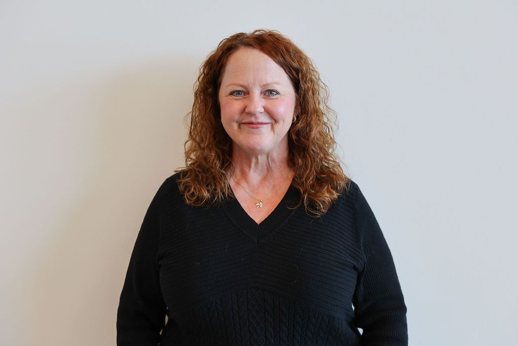 Woman in blue shirt smiles in front of a white wall.