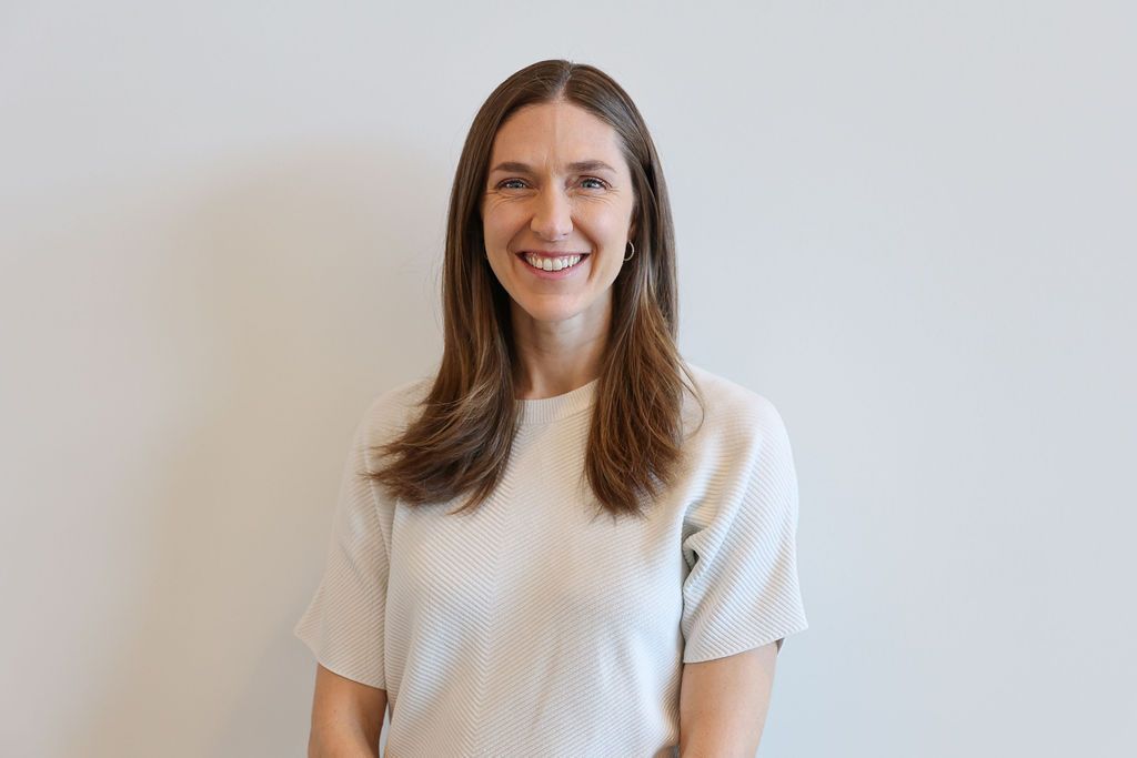 Woman with long brown hair smiling, wearing a light-colored blazer and shirt.