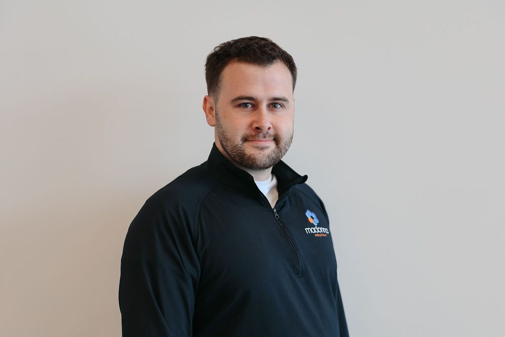 Man with dark hair and beard, wearing a navy blue jacket, standing against a neutral wall.