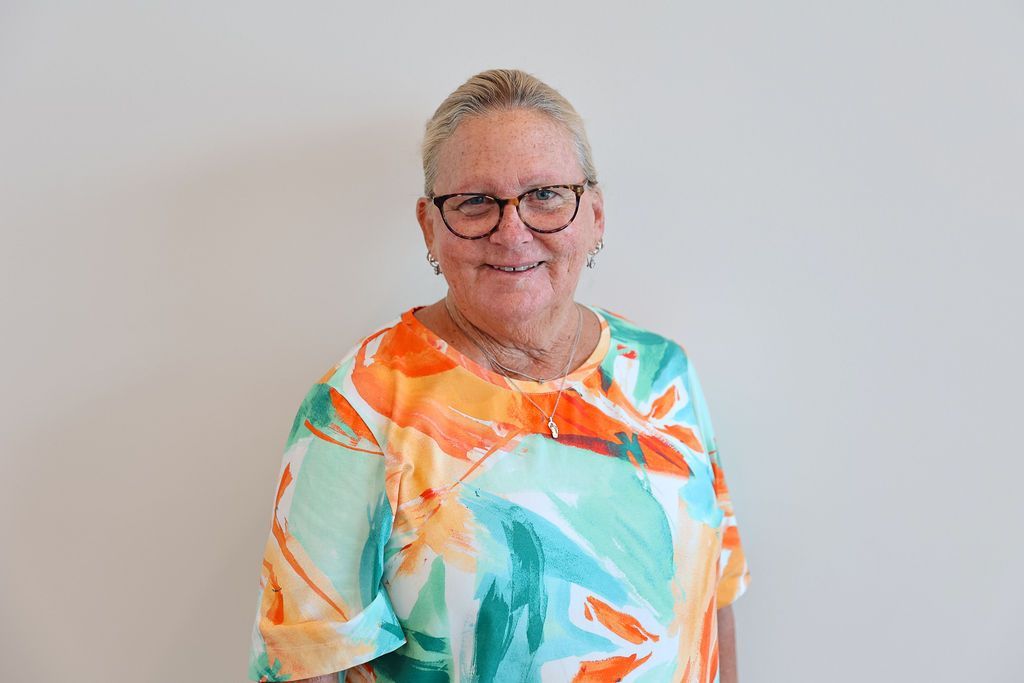 Woman with glasses smiles, wearing a colorful orange and teal patterned top.