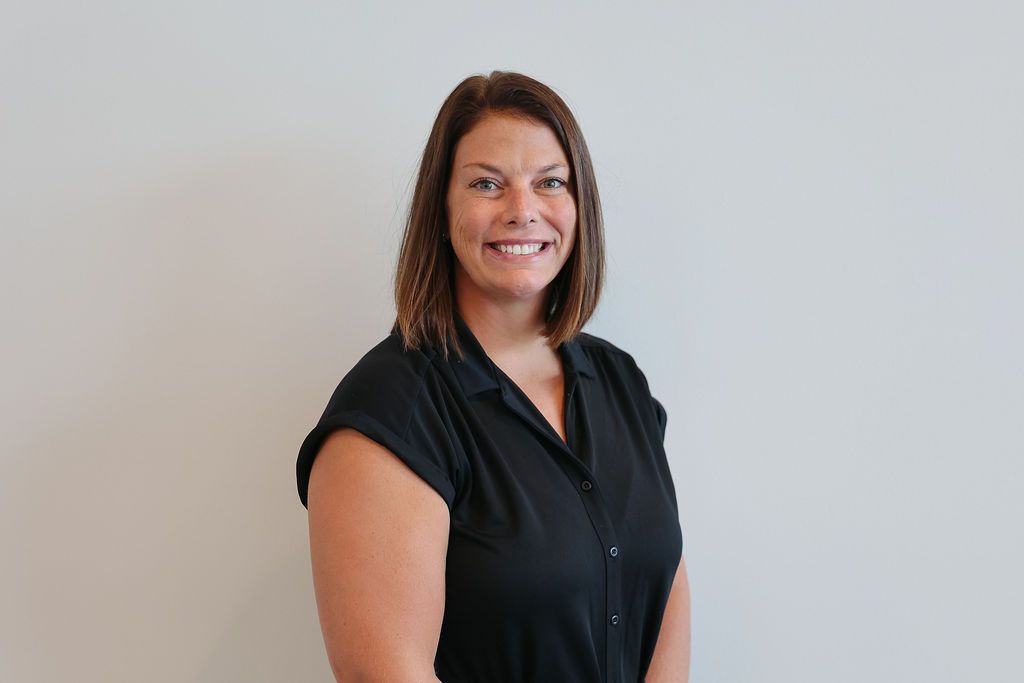 Woman smiling, wearing a black top, against a white wall.