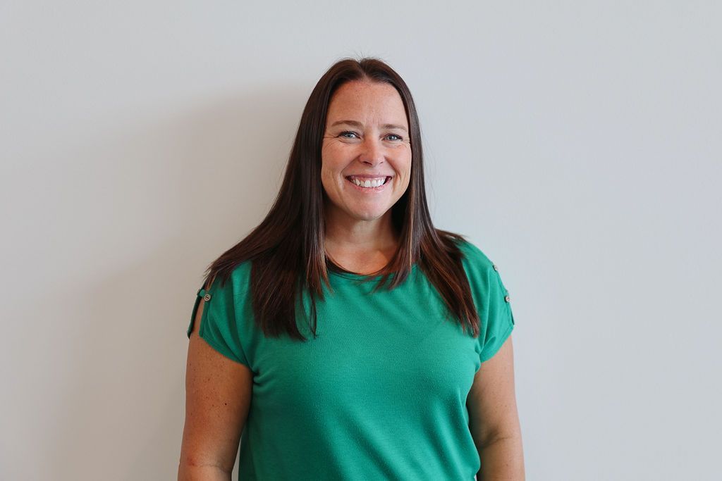 Woman in a green shirt smiling in front of a white wall.