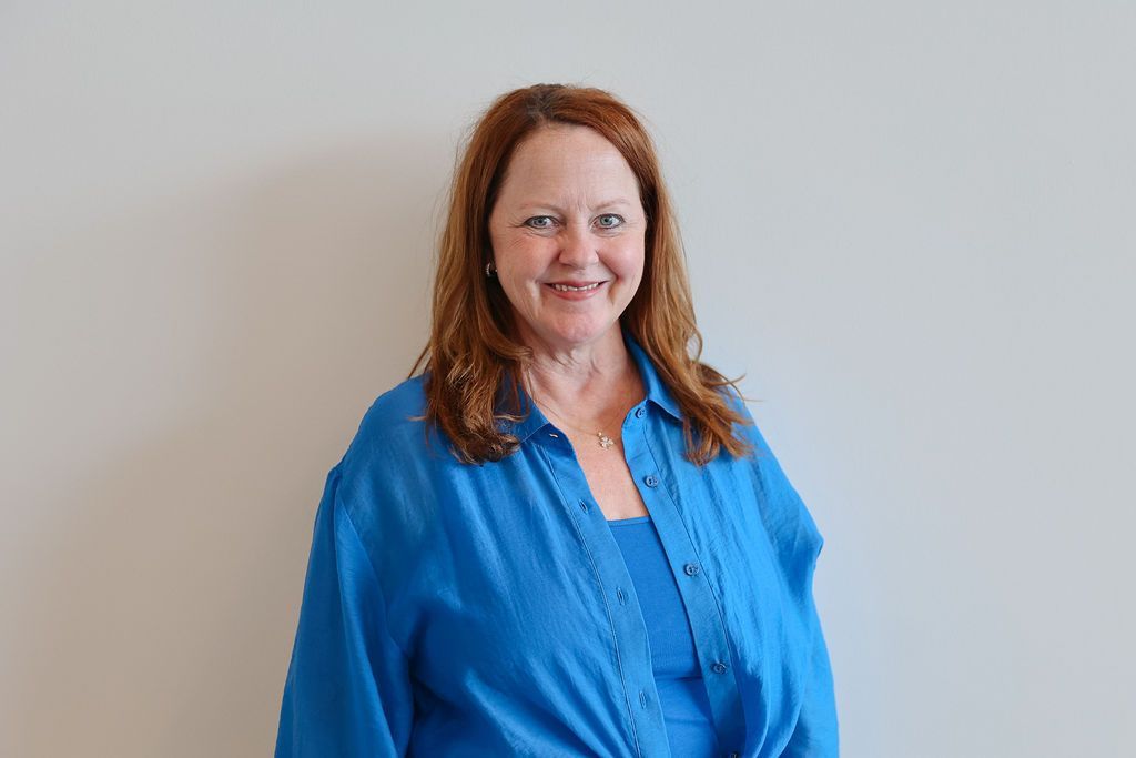 Woman in blue shirt smiles in front of a white wall.