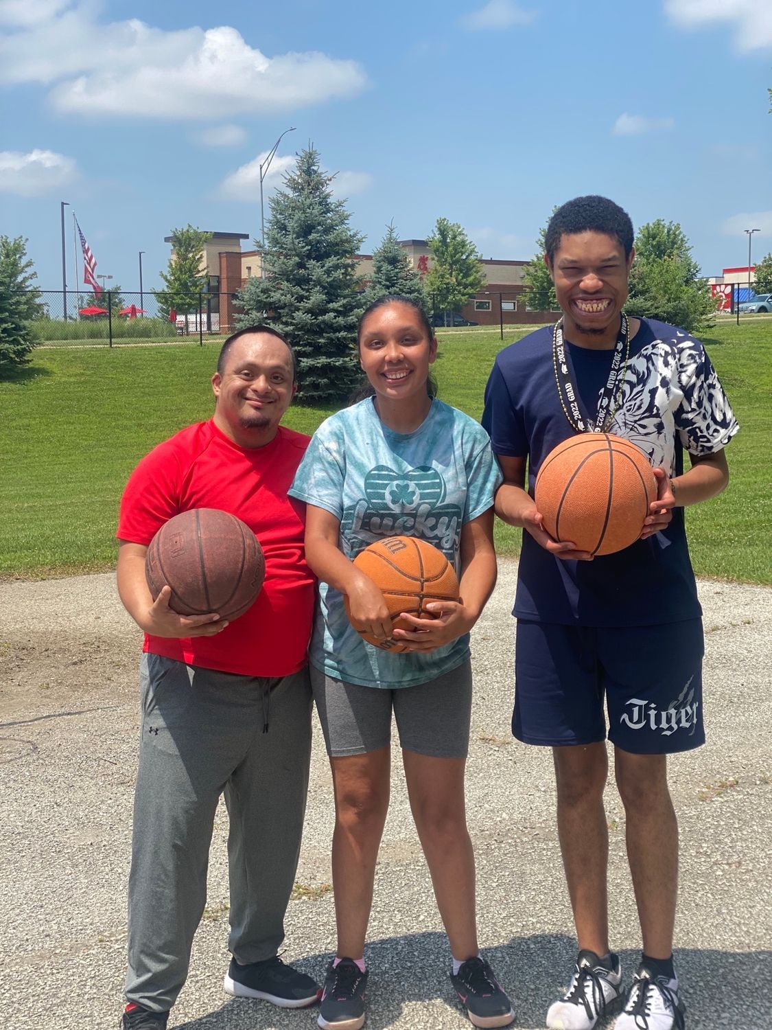 Three people hold basketballs outside; sunny day.