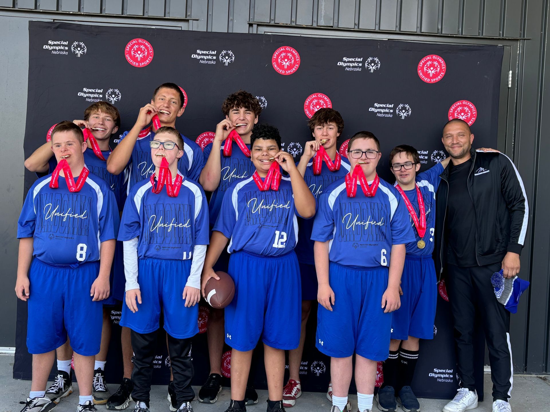 Football team in blue uniforms with medals posing in front of a backdrop, some holding up medals.