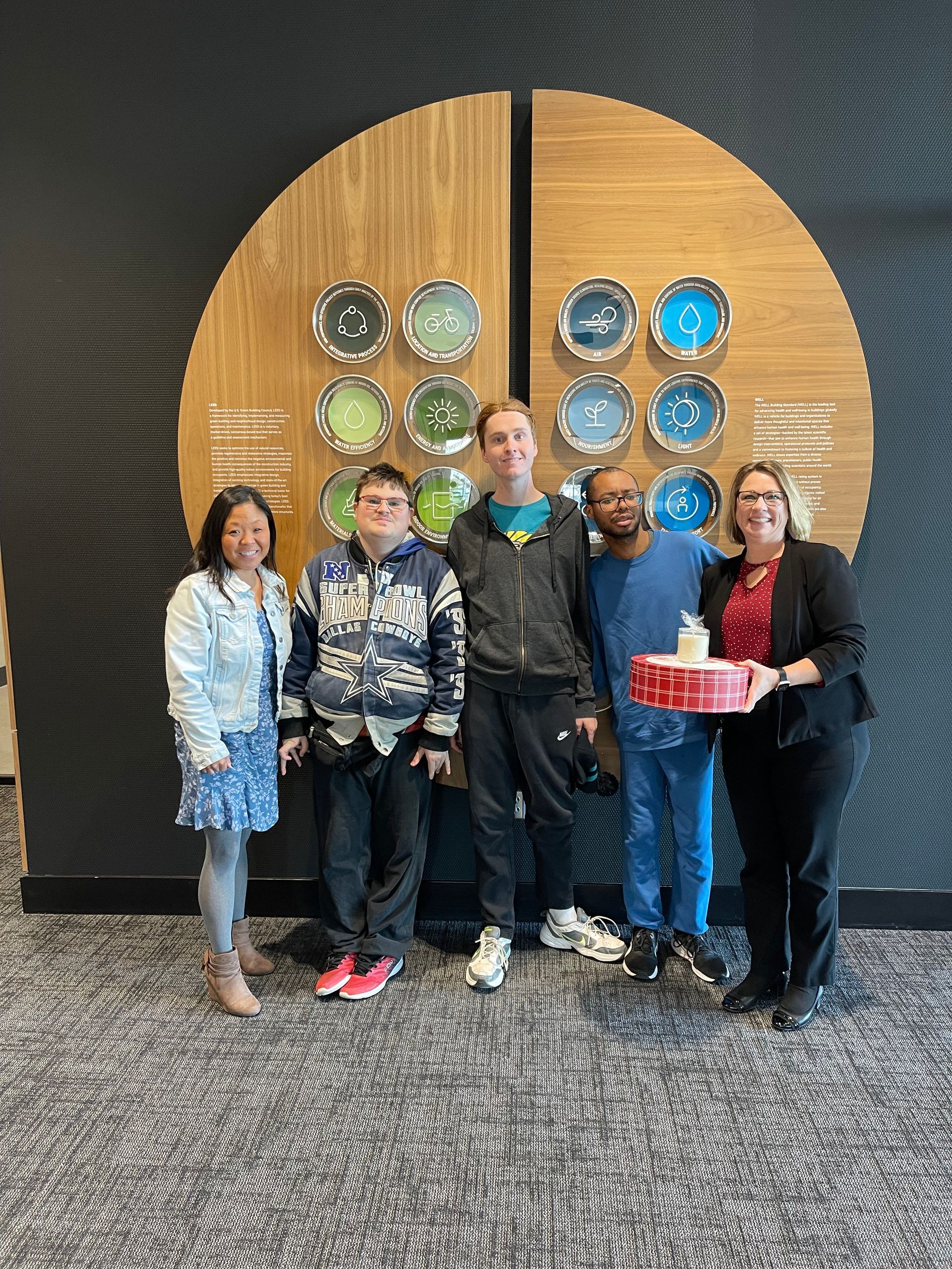 Five people stand in front of a circular wall display. One holds a box.