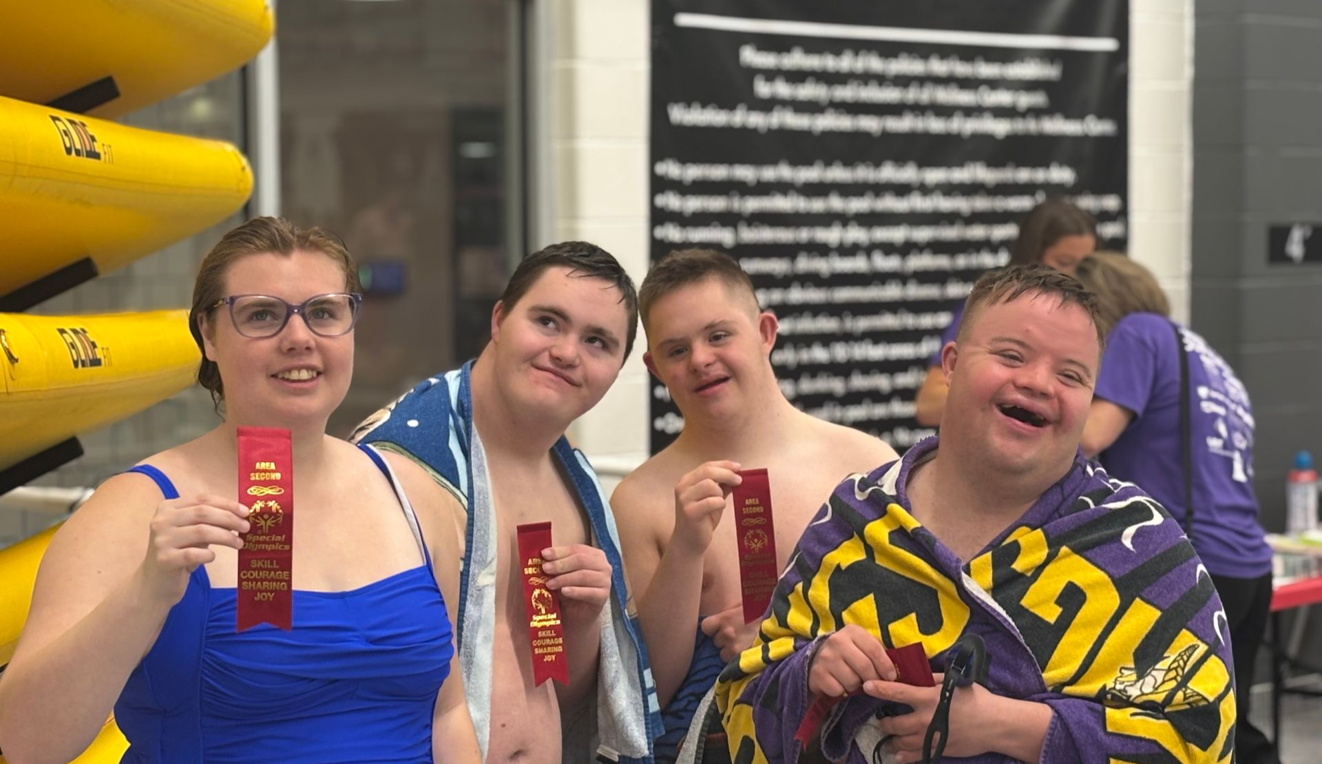 Four people with Down syndrome in a pool, holding red ribbons, smiling.
