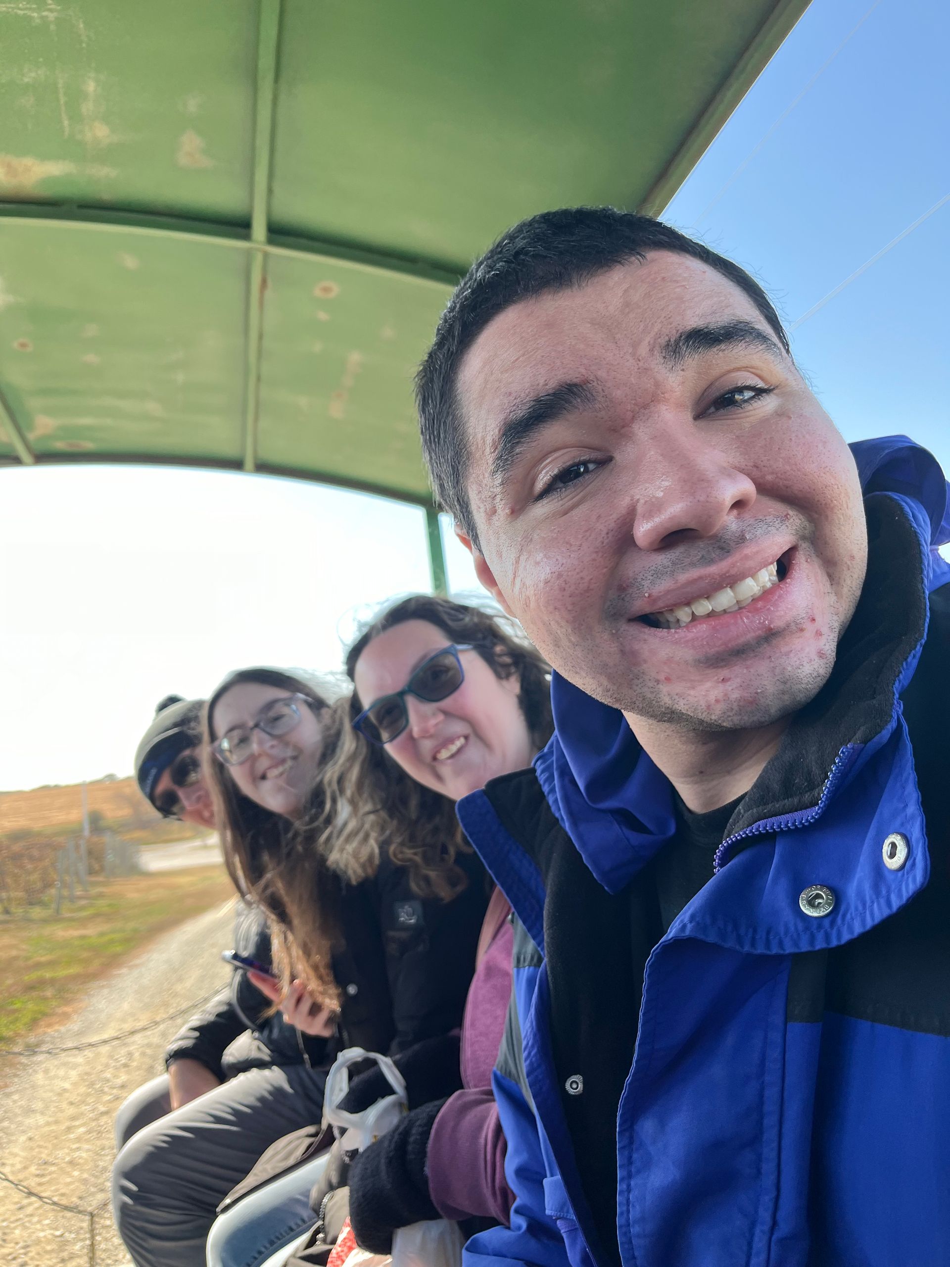 People smiling, riding on a covered wagon on a sunny day.