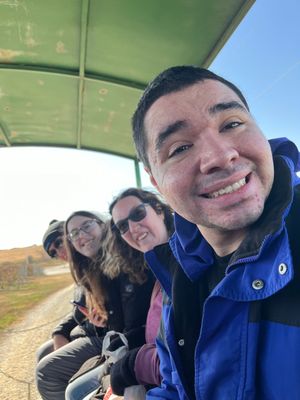People smiling, riding on a covered wagon on a sunny day.