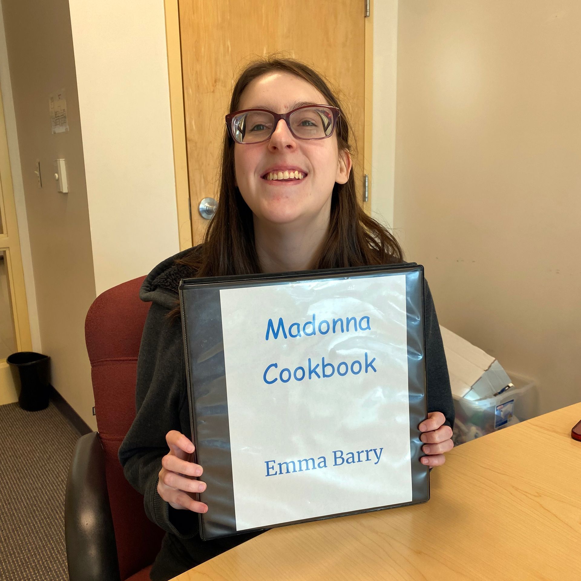 Person smiles, holding a binder labeled 