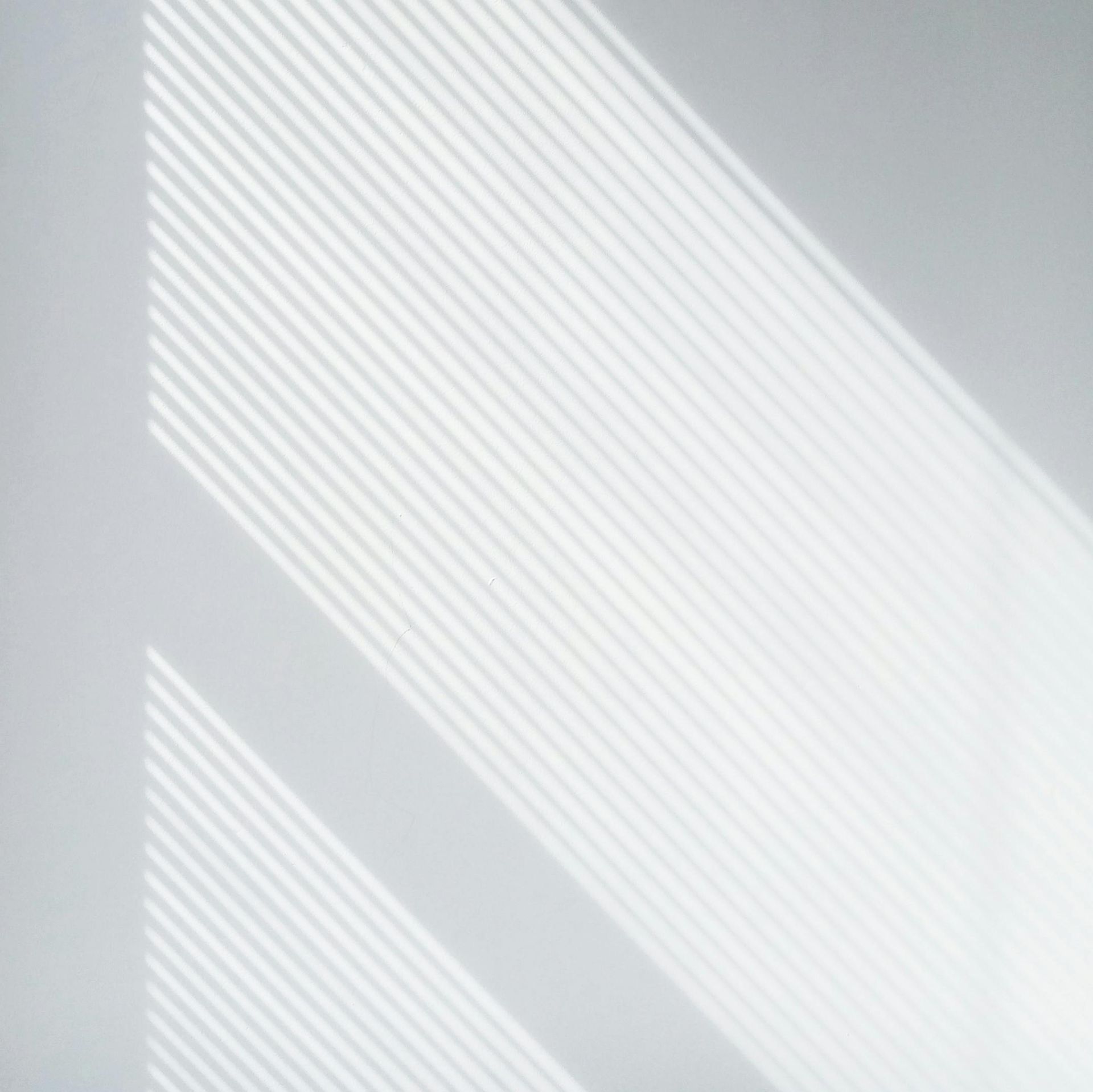Shadows of horizontal blinds cast across a white wall, creating a striped pattern.