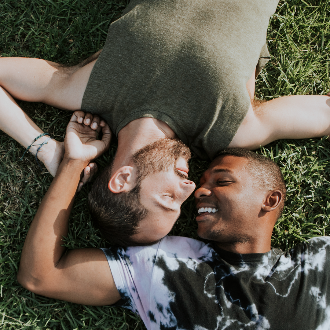 Two men are laying on their backs in the grass looking at each other.