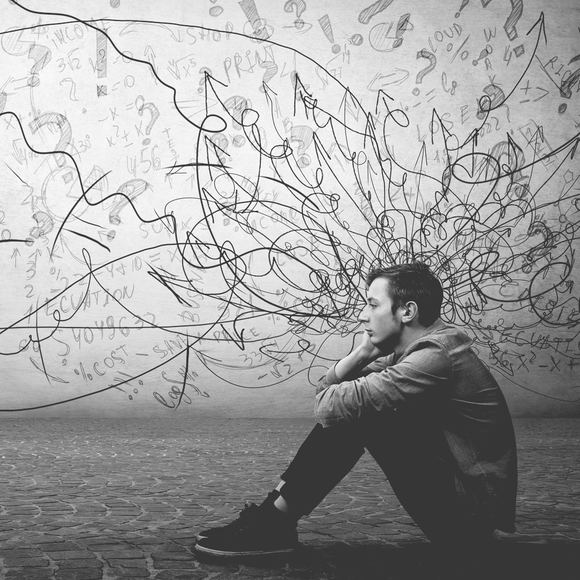 A man is sitting on the floor in front of a wall with drawings on it.