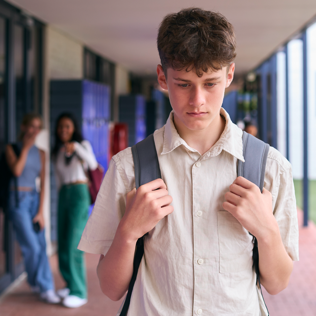 A young man with a backpack is walking down a hallway.
