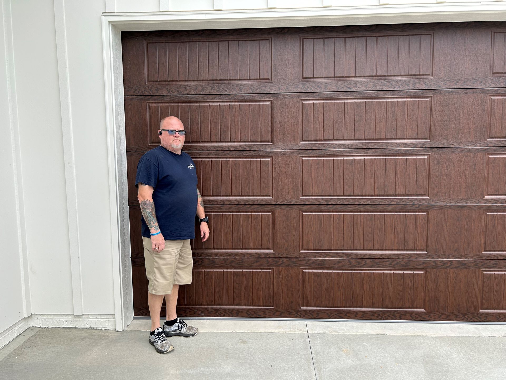 A man is standing in front of a brown garage door.