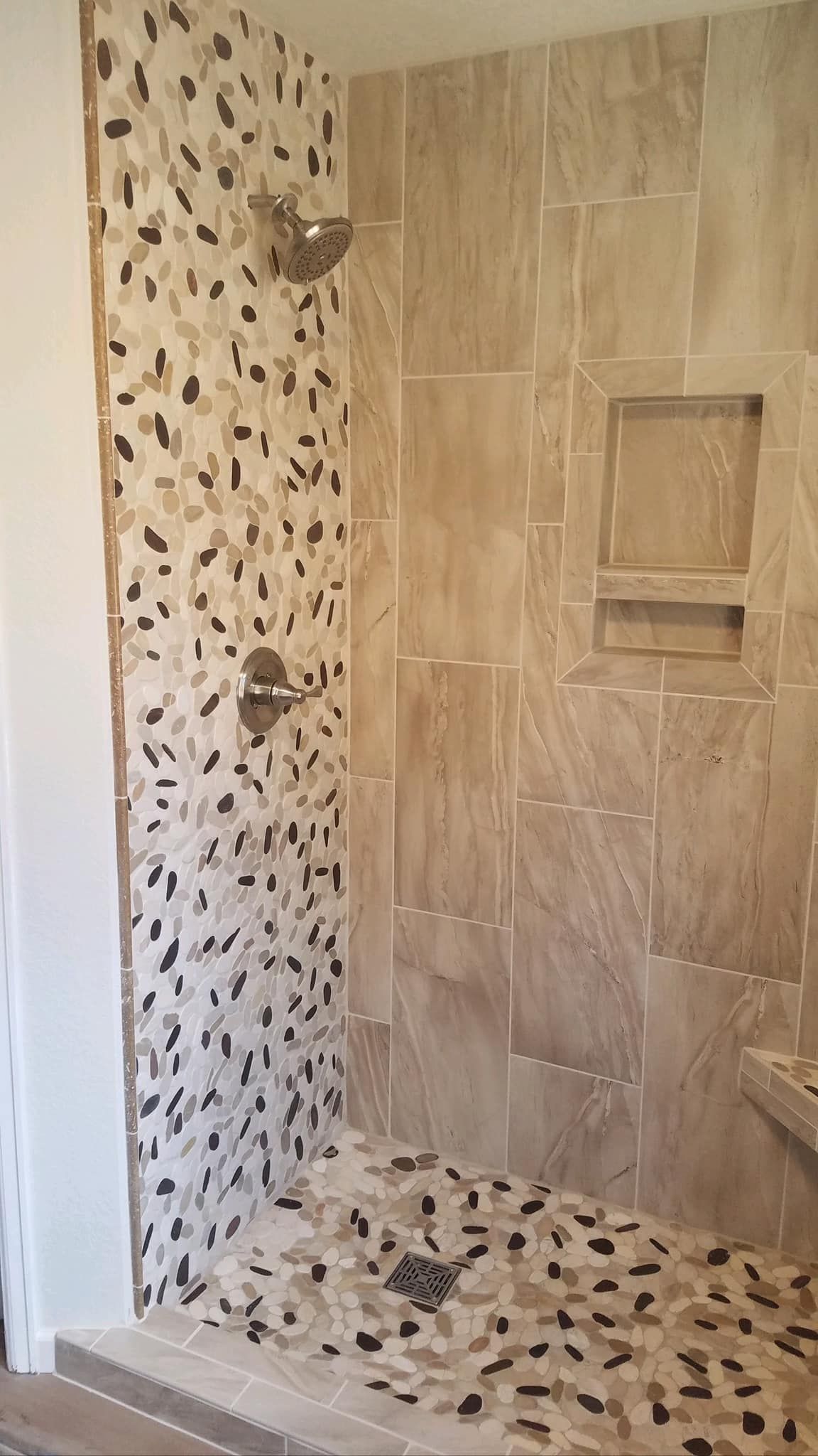 A walk in shower with a tiled wall and a mosaic floor.