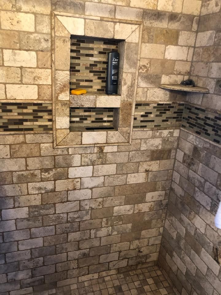 A shower with a bottle of shampoo in a niche.