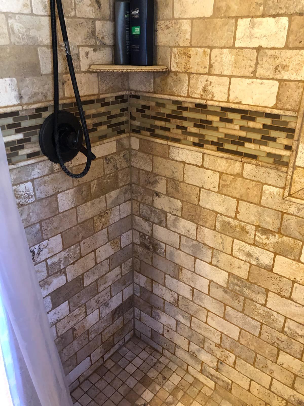 A shower with a brick wall and a tiled floor.