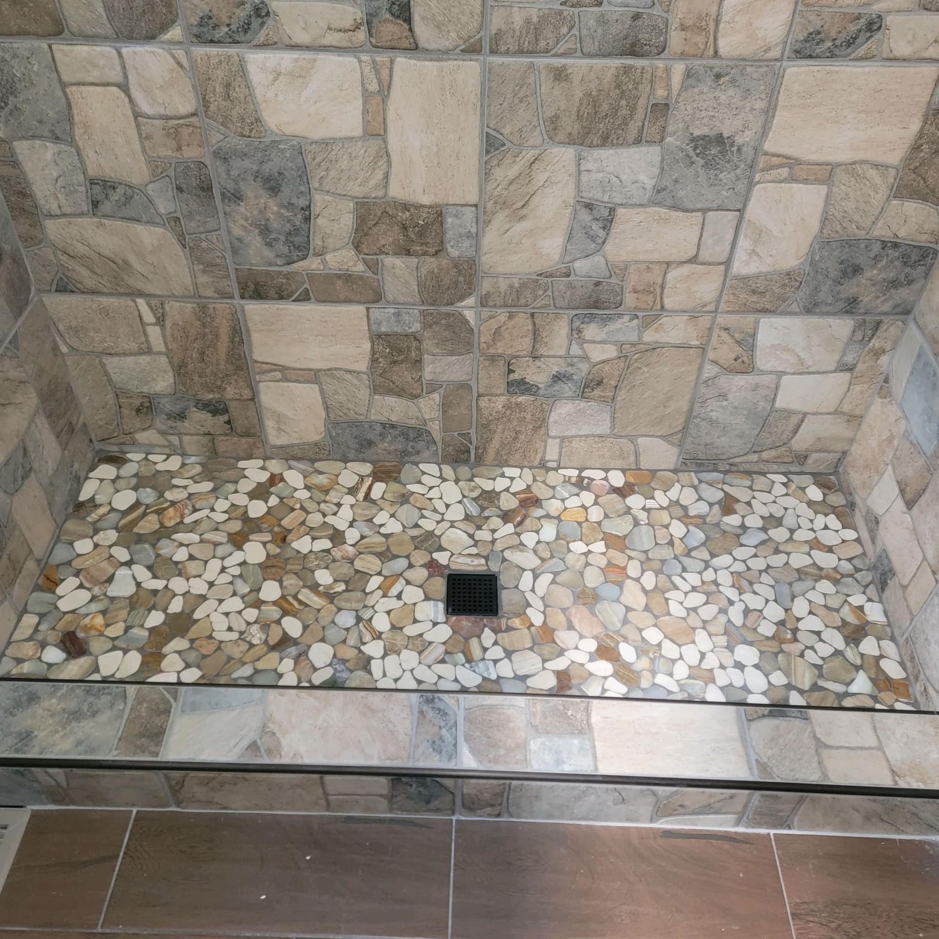 a walk in shower with a ceramic tiled wall and a stone floor