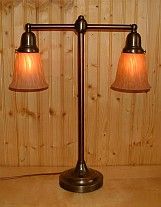 Bronze table lamp with two shaded lights, set against a wood backdrop.