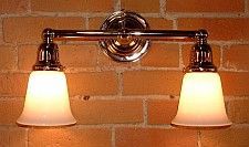 Two-bulb bathroom light fixture with frosted glass shades, mounted on a brick wall.