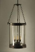 Lantern with clear glass cylinder, three candelabra bulbs, and dark metal frame suspended from chains.