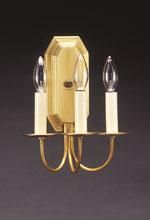 Brass wall sconce with three candle-shaped bulbs on a dark background.