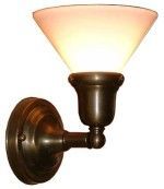 Wall-mounted sconce with bronze finish, holding a white, inverted cone-shaped shade, lit with warm light.