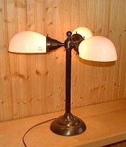 Bronze desk lamp with three white, dome-shaped shades, on a wooden surface.