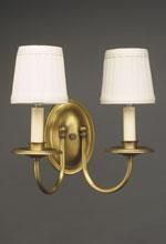 Wall-mounted, brass-toned sconce with two candle-style lights, each topped with a white lampshade.